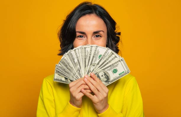 A smiling woman holding a fan of hundred-dollar bills